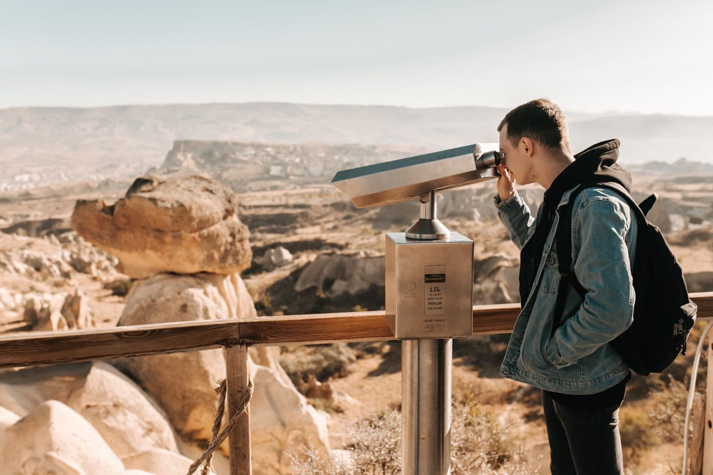 A man looking through a telescope on a rocky landscape at dusk