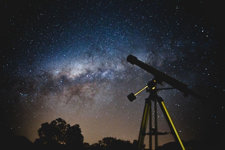 A telescope silhouetted against the Milky Way in a starry sky