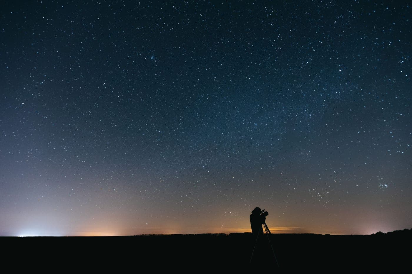 A person using an optical instrument beneath a vast star-filled sky