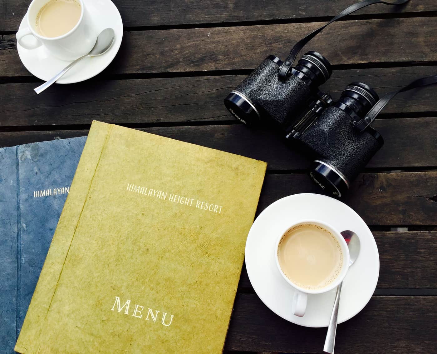 A pair of binoculars resting on a wooden table beside a coffee cup