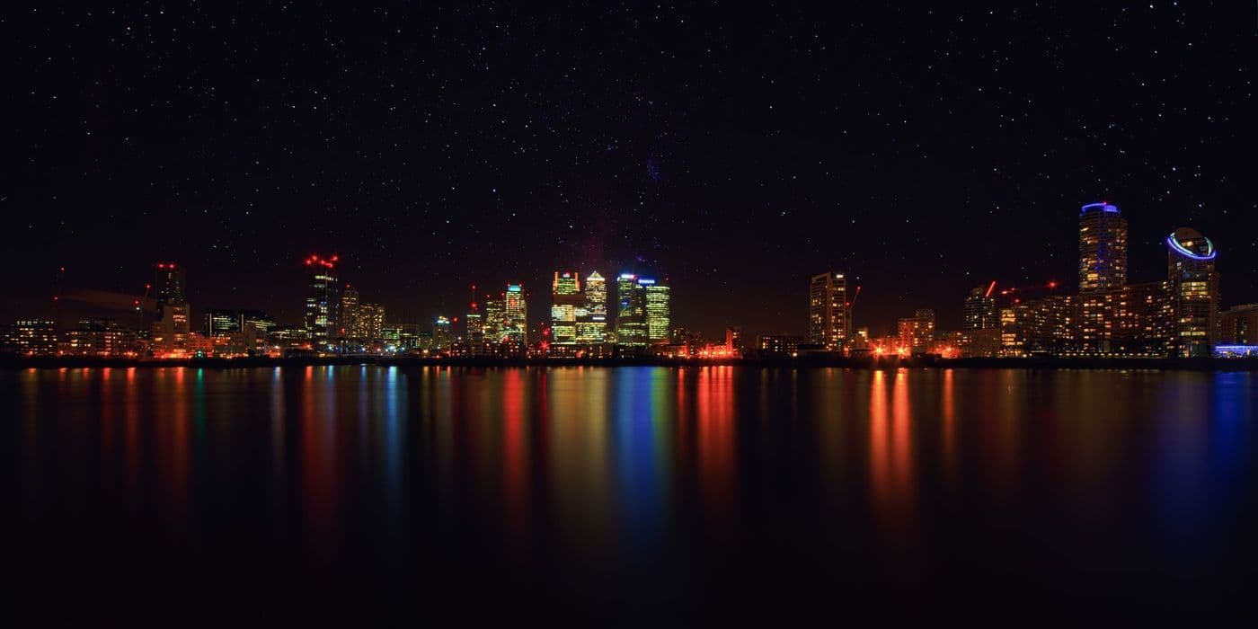 A city skyline at night reflected in water beneath a starry sky