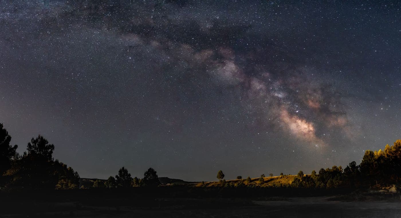 A wide-field photograph of the Milky Way arching over a dark landscape