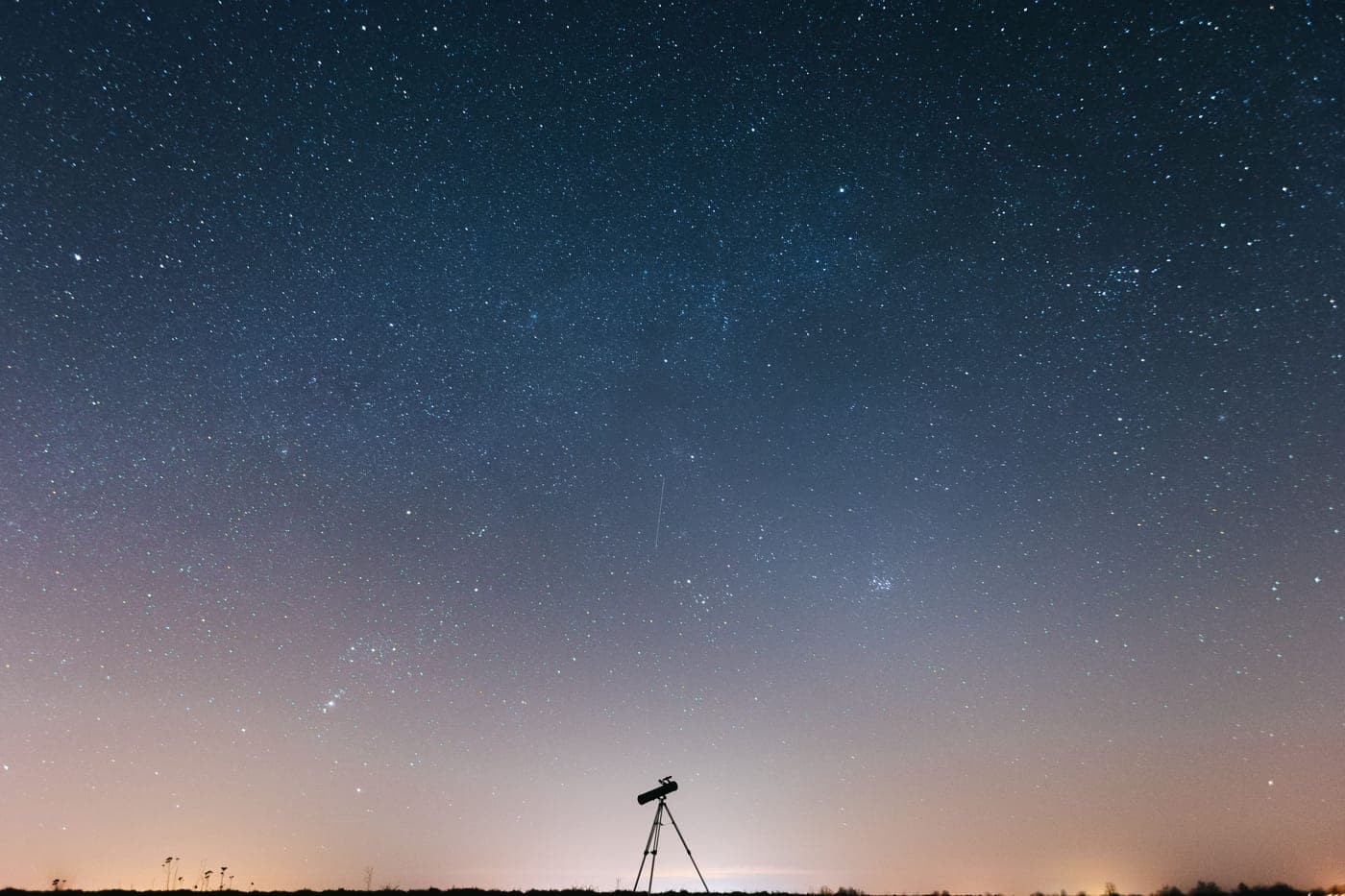 A telescope silhouetted against a sky full of stars