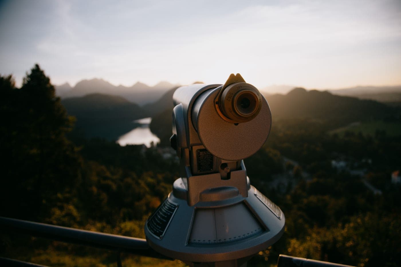 A telescope set up on a balcony overlooking wooded hills
