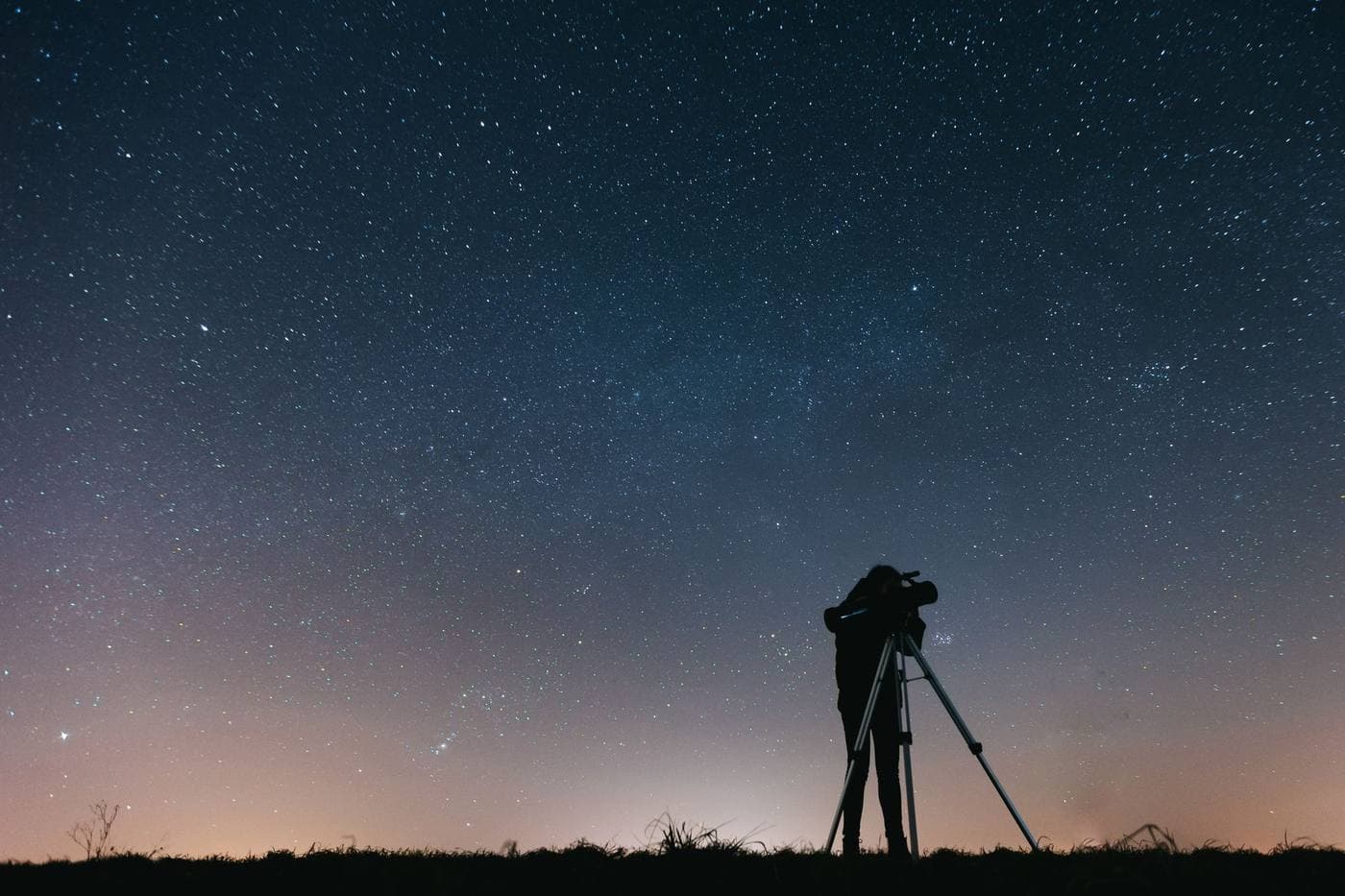 A person at a telescope silhouetted against a sky full of stars