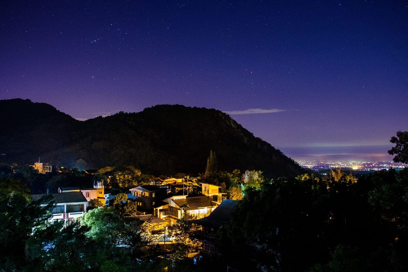 An illuminated village under a starry sky with mountains behind it