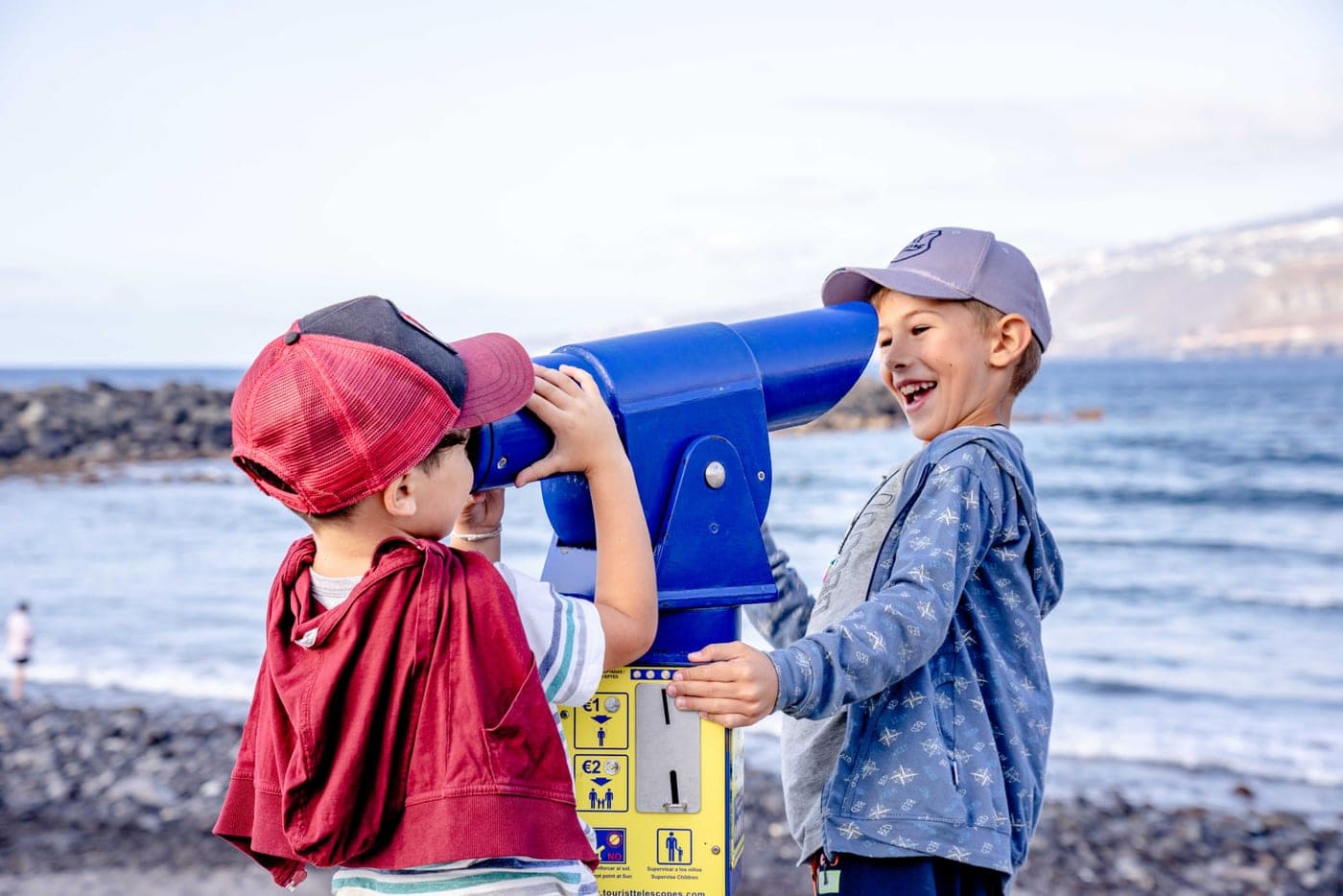 Two children using a telescope together beside the sea