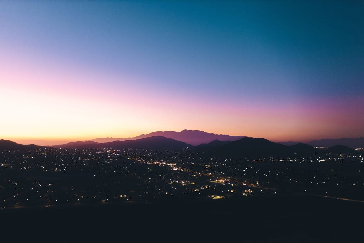 A brightly lit city below a mountain silhouette at twilight