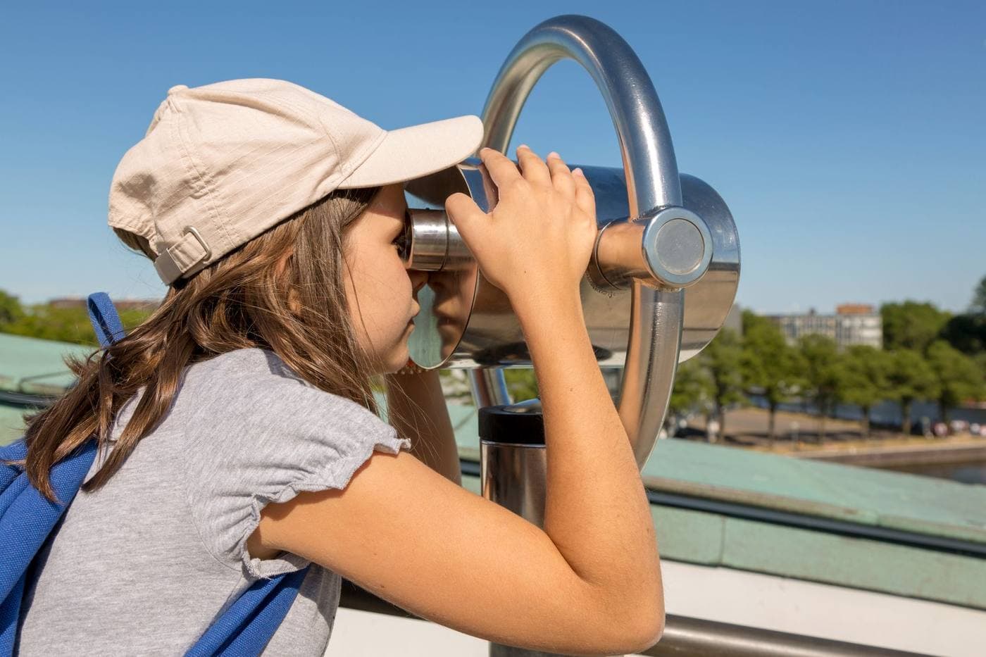 A young girl using a telescope outdoors on a bright day