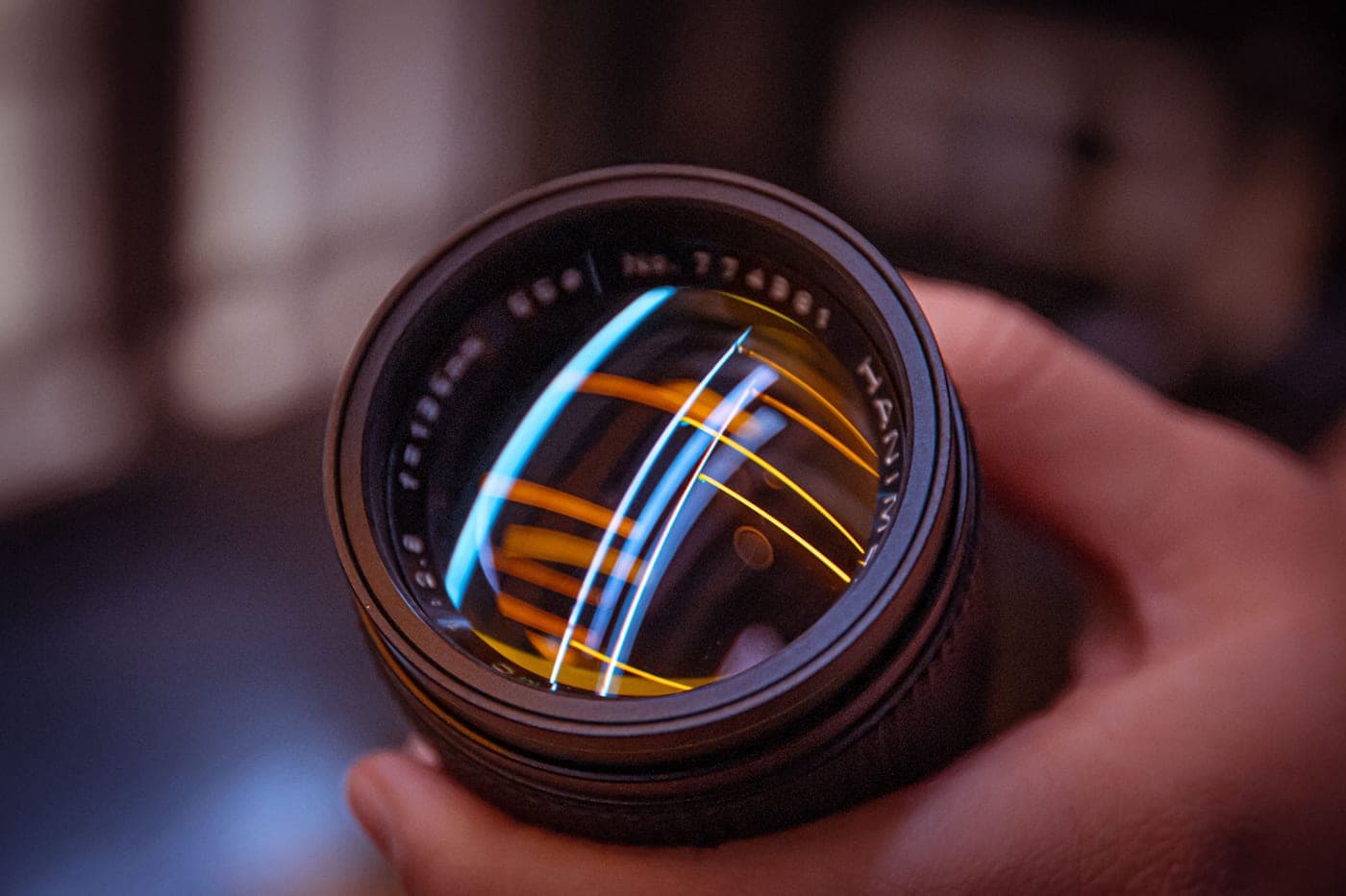 A hand holding a lens, with colored light reflecting off the glass