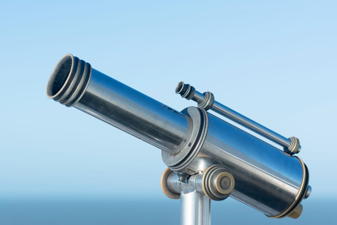 A metal coin-operated viewing telescope pointing into a clear blue sky