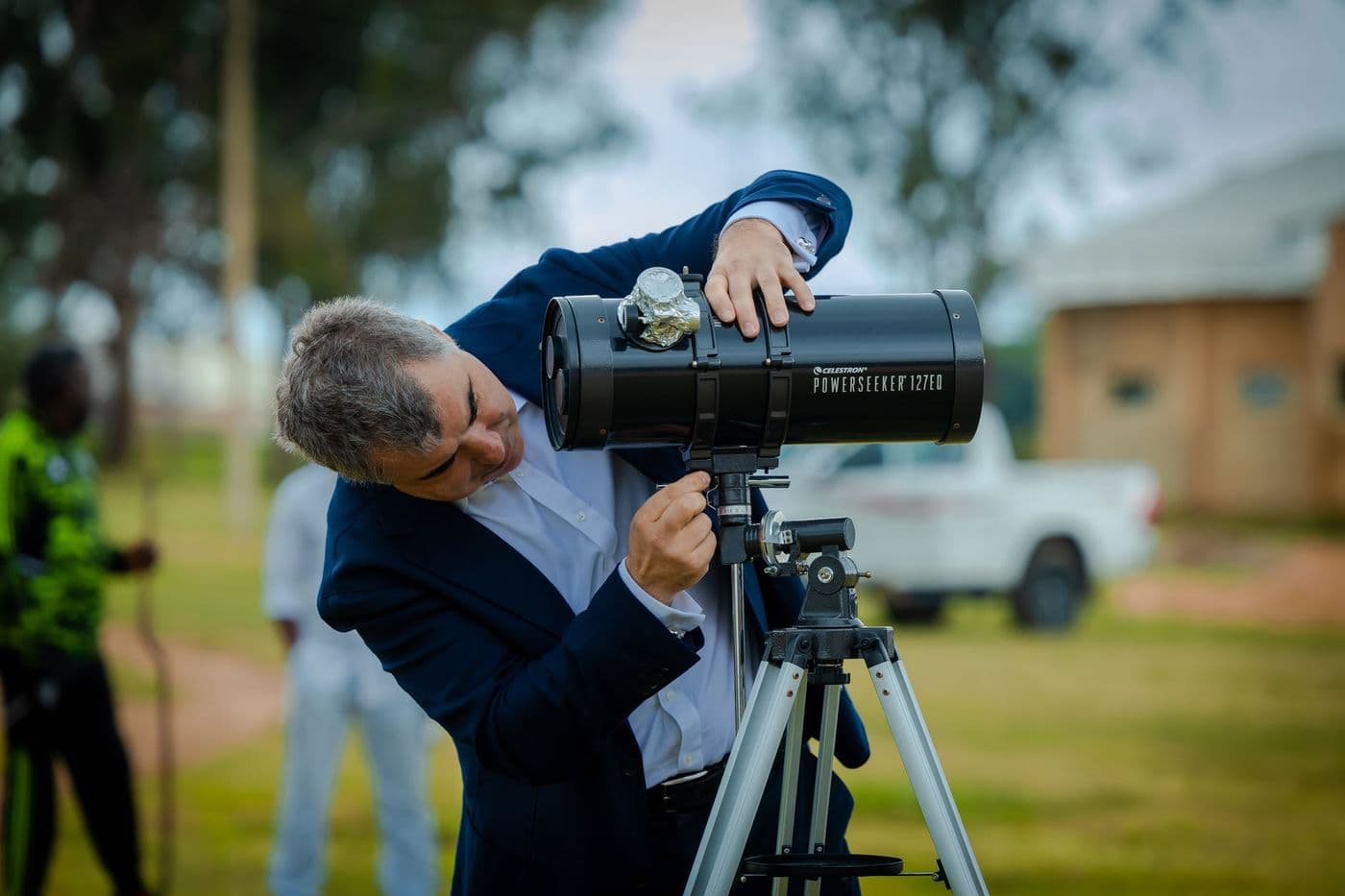 A man using a telescope on a tripod outdoors in daylight
