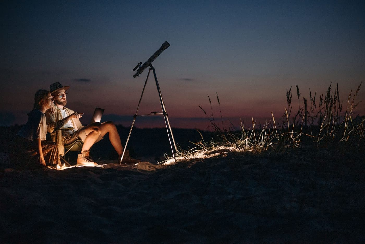 Two people using a telescope outdoors at twilight