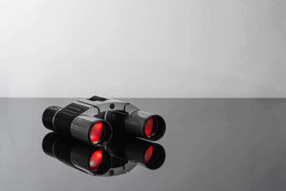 Close-up of modern binoculars, their coated lenses reflecting the light