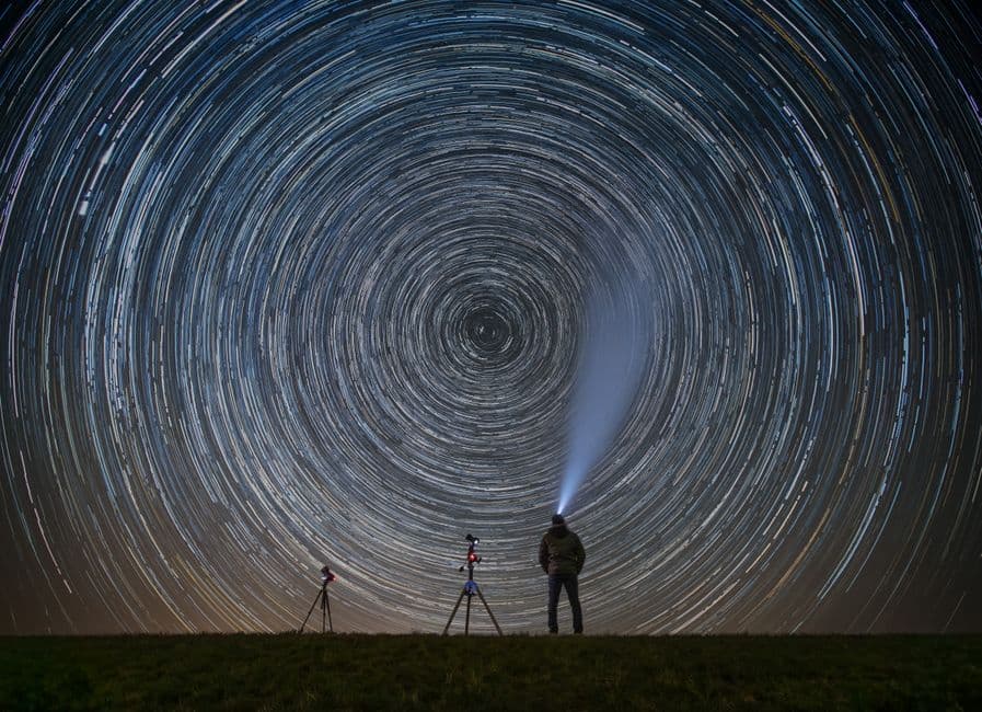 A lone stargazer with a flashlight standing beneath long star trails