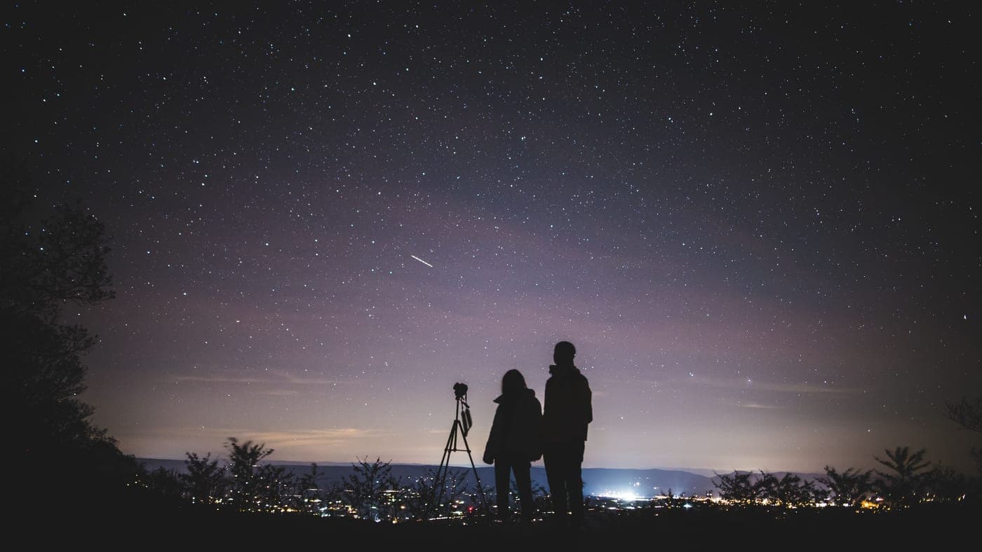 Two people stargazing under a dense field of stars