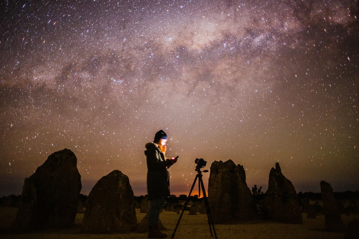 A photographer with a camera on a tripod under a starry sky