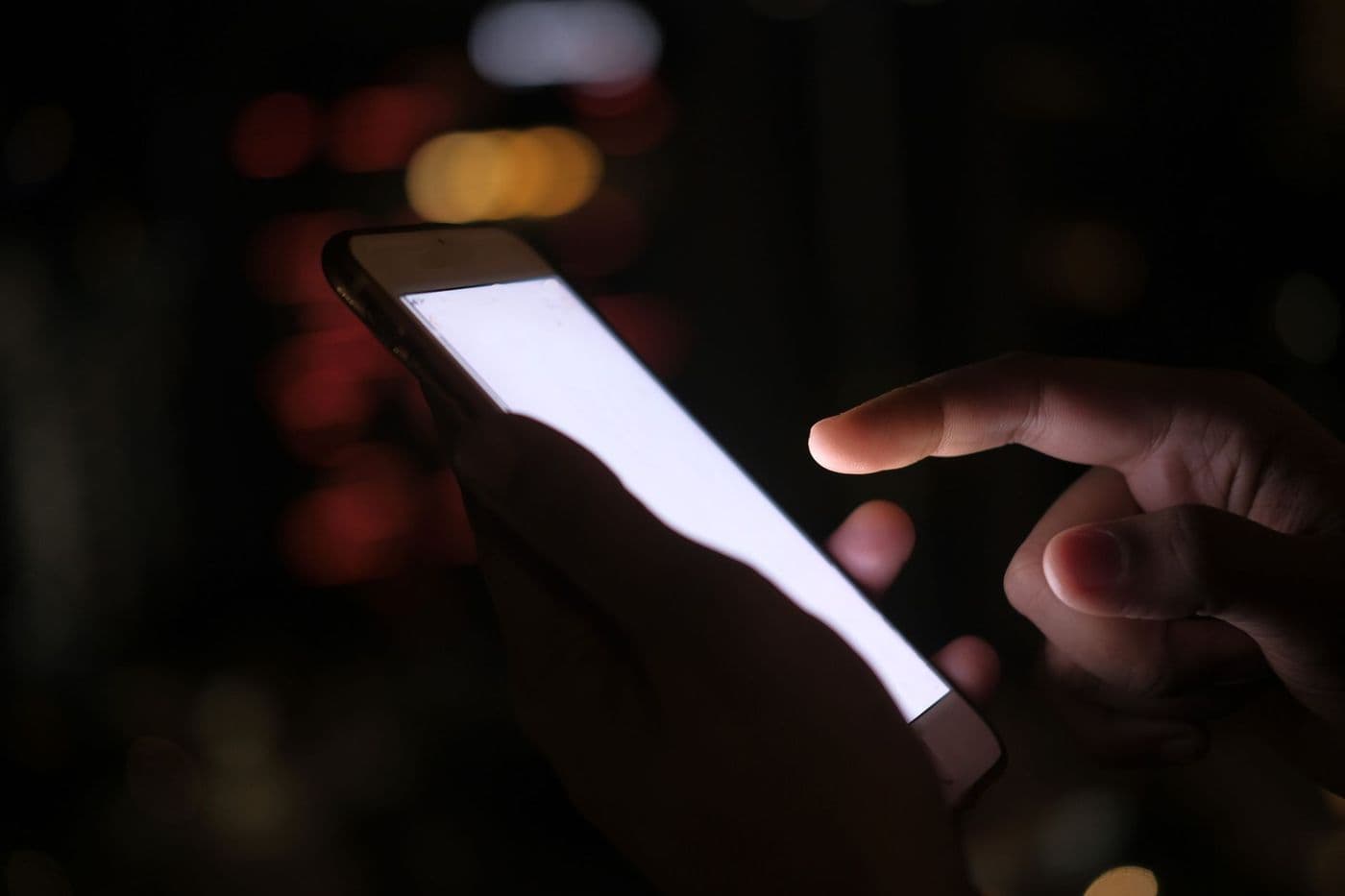 A hand holding a lit smartphone in the dark against blurred city lights