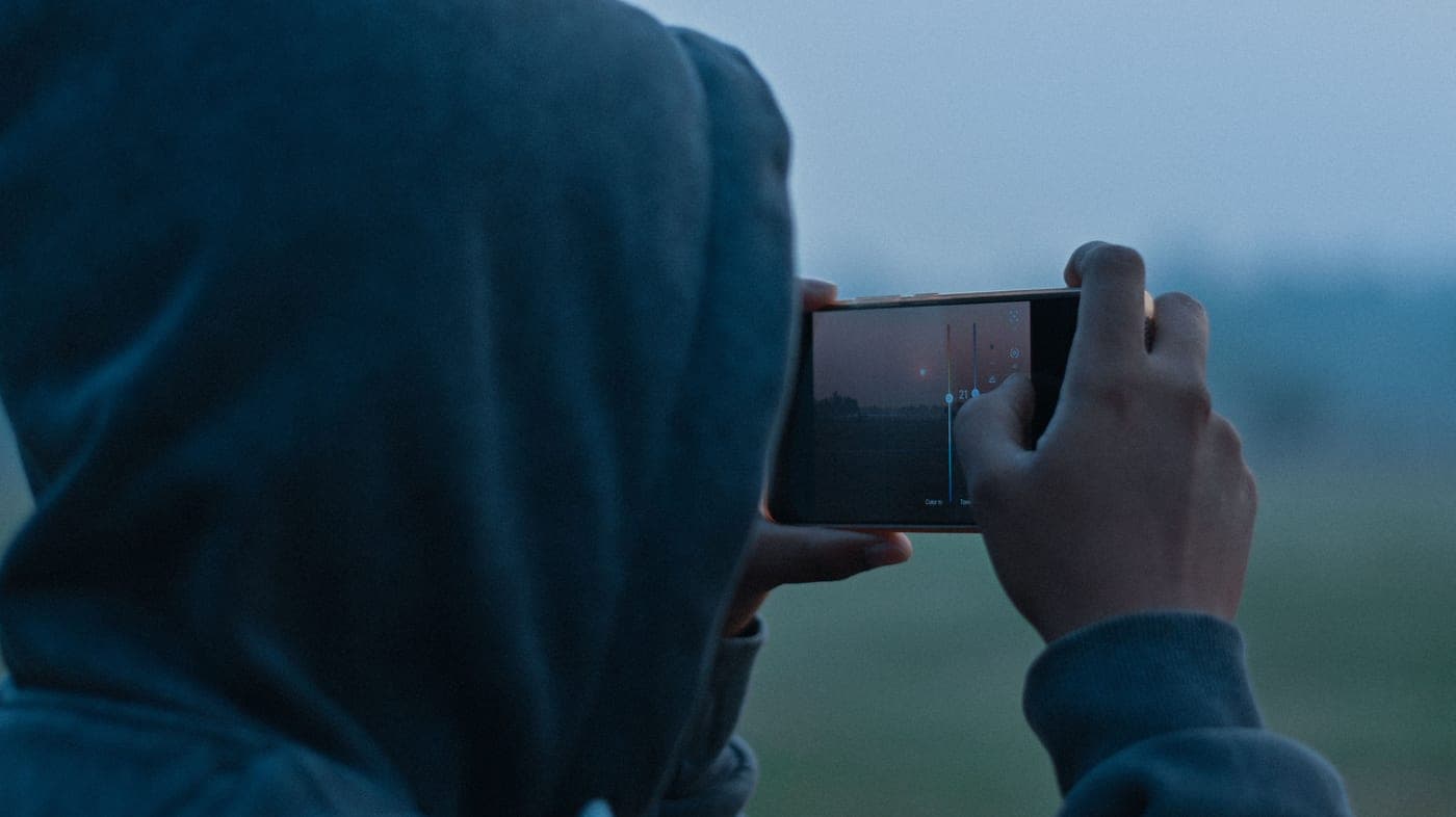 A person holding up a smartphone against an outdoor scene at twilight