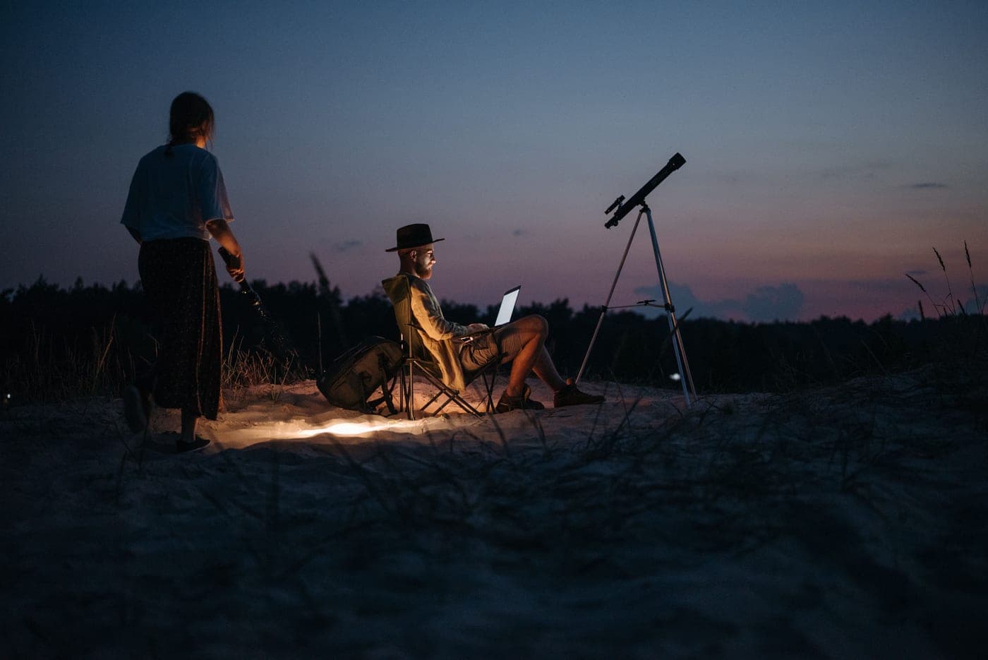 Two people at a campsite at night with a telescope