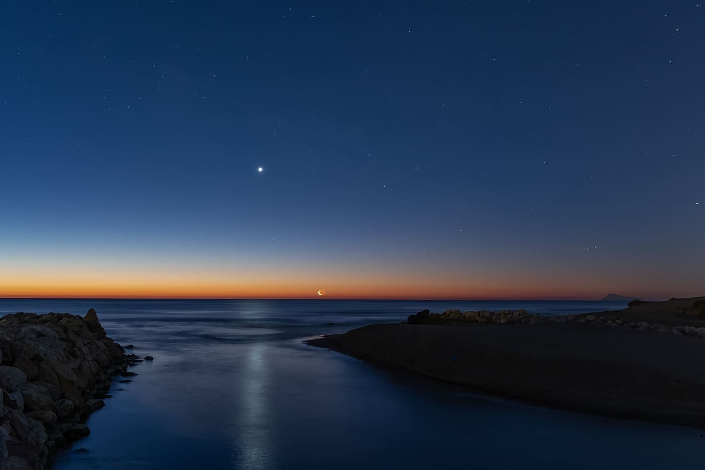A crescent moon and a single brilliant point of light low in a twilight sky