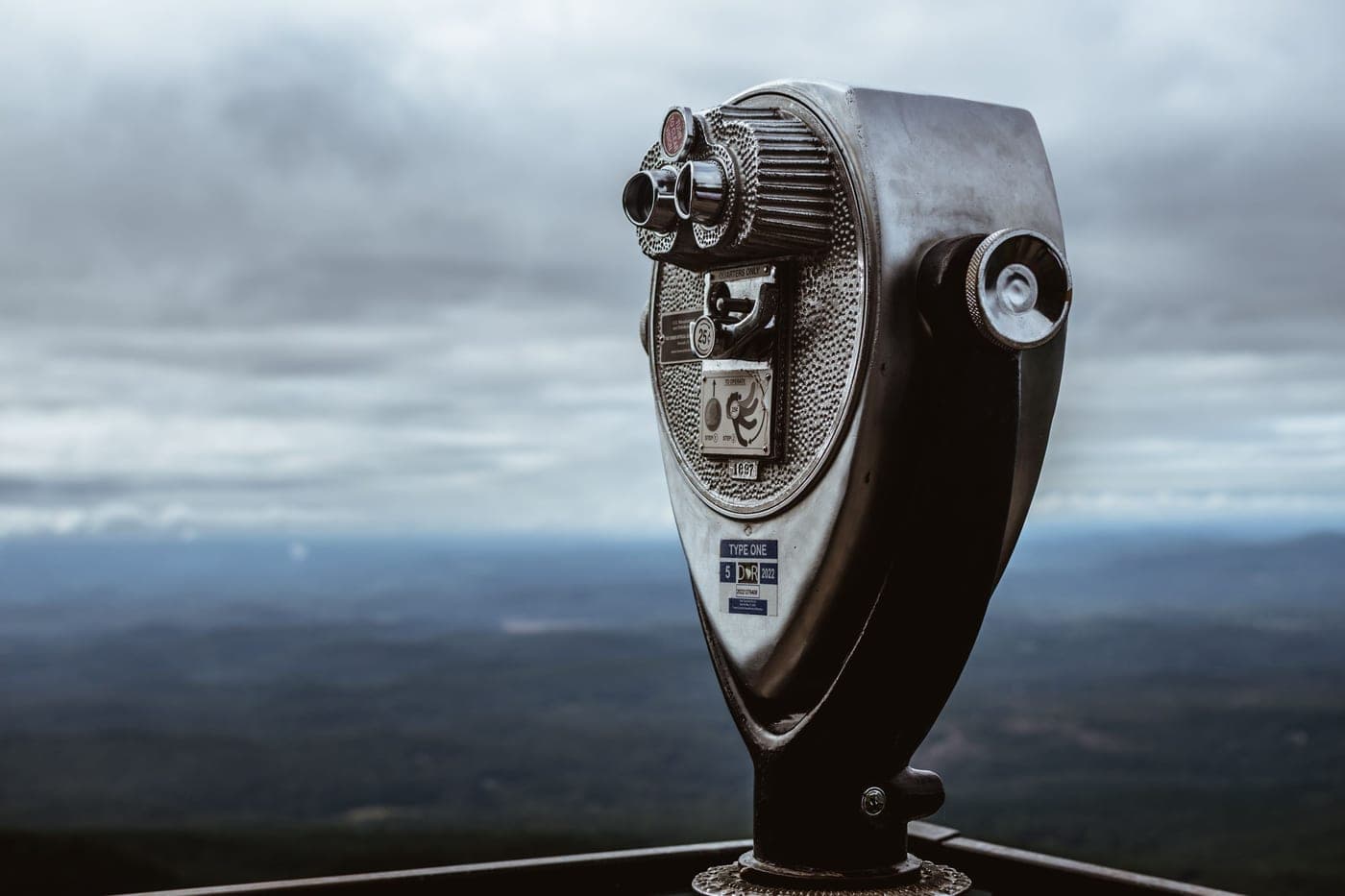 A mounted viewing telescope on a mountain under a cloudy sky