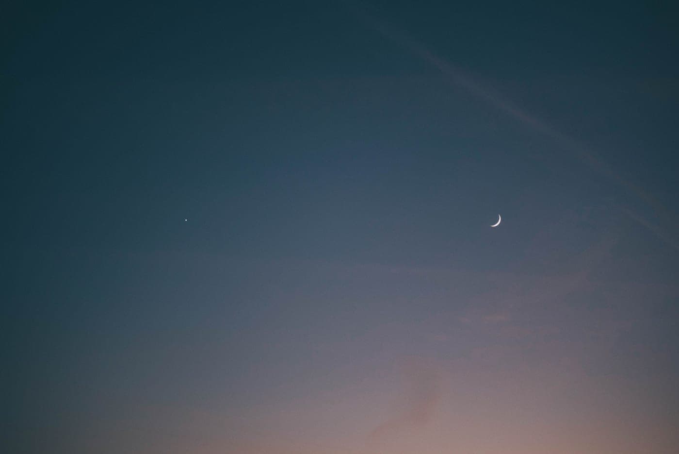 A crescent moon and a single bright point of light in an evening sky